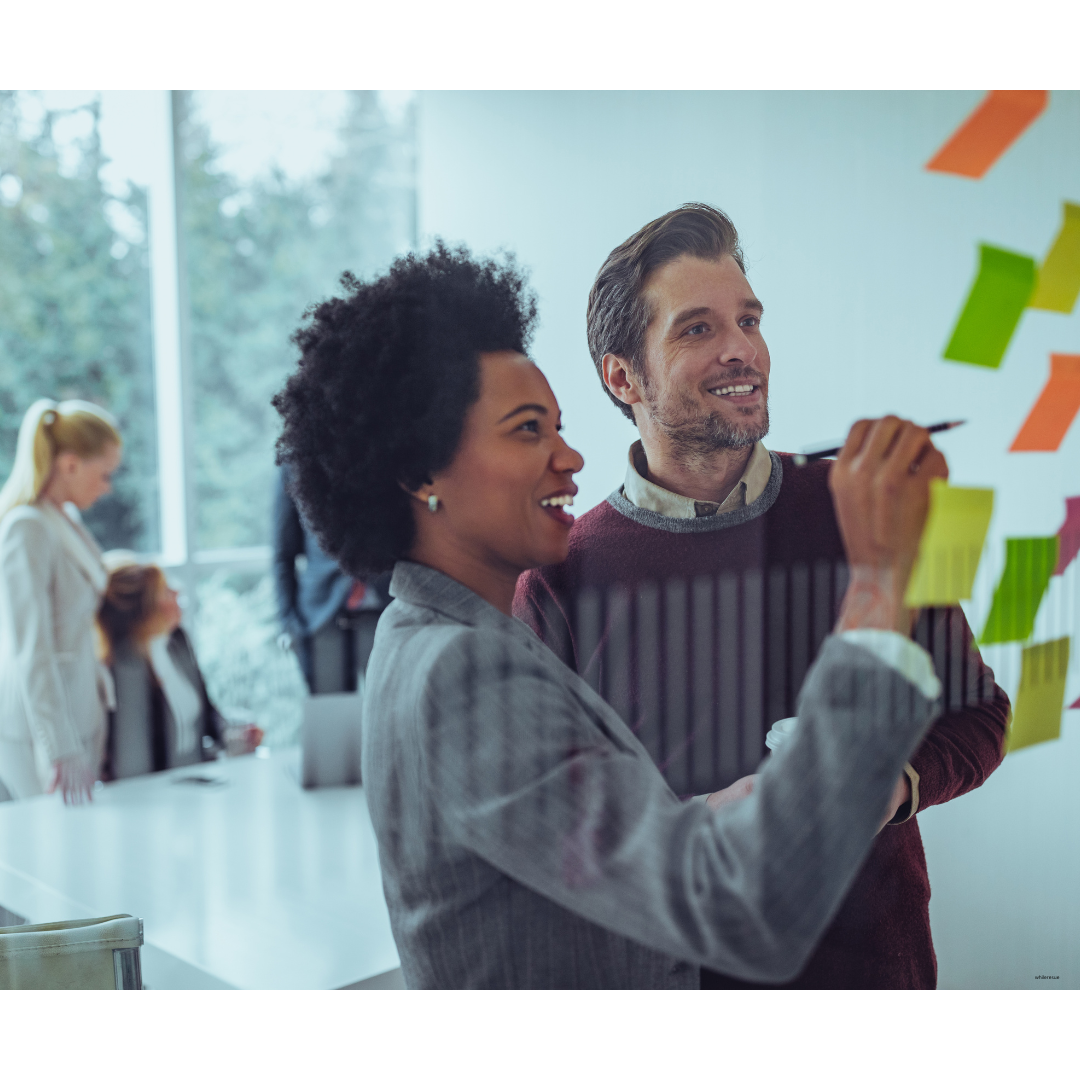 Two smiling professionals collaborating in front of a wall of colorful post-its during a team brainstorming session